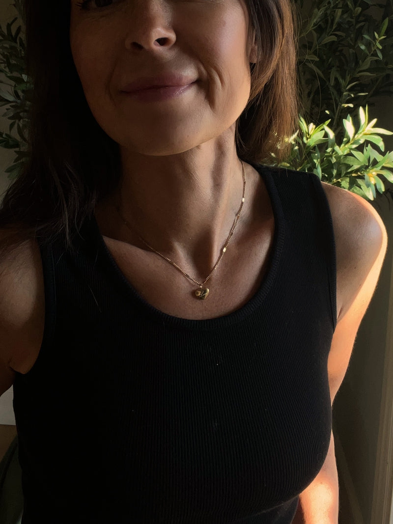 smiling woman wearing a golden heart necklace with the word love on it. perfect for layering