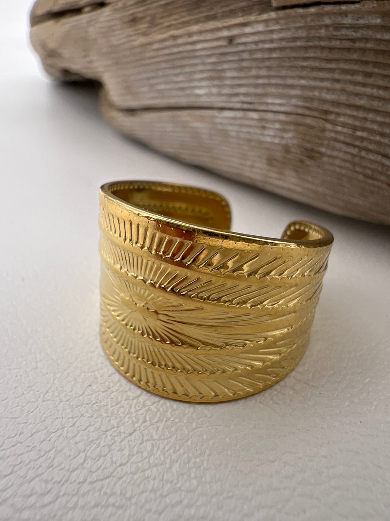 Gold cuff ring with sun design on a textured surface