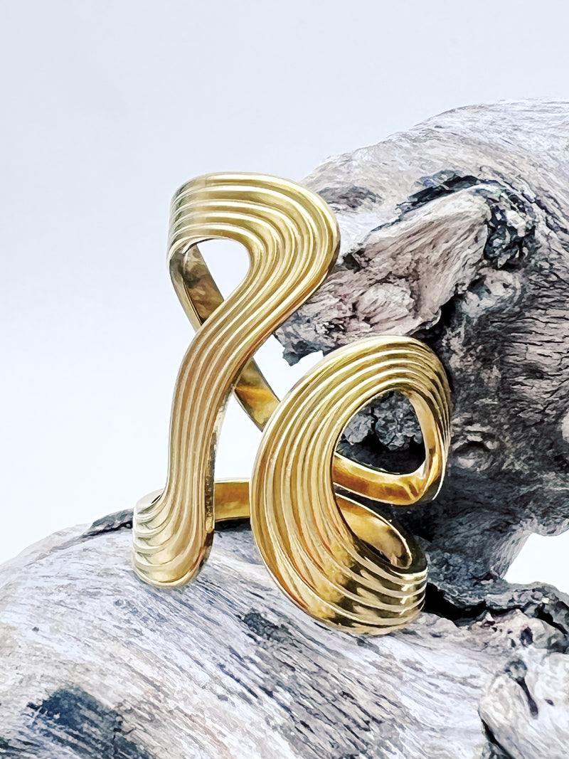 Gold ring with a wavy design on a wooden surface