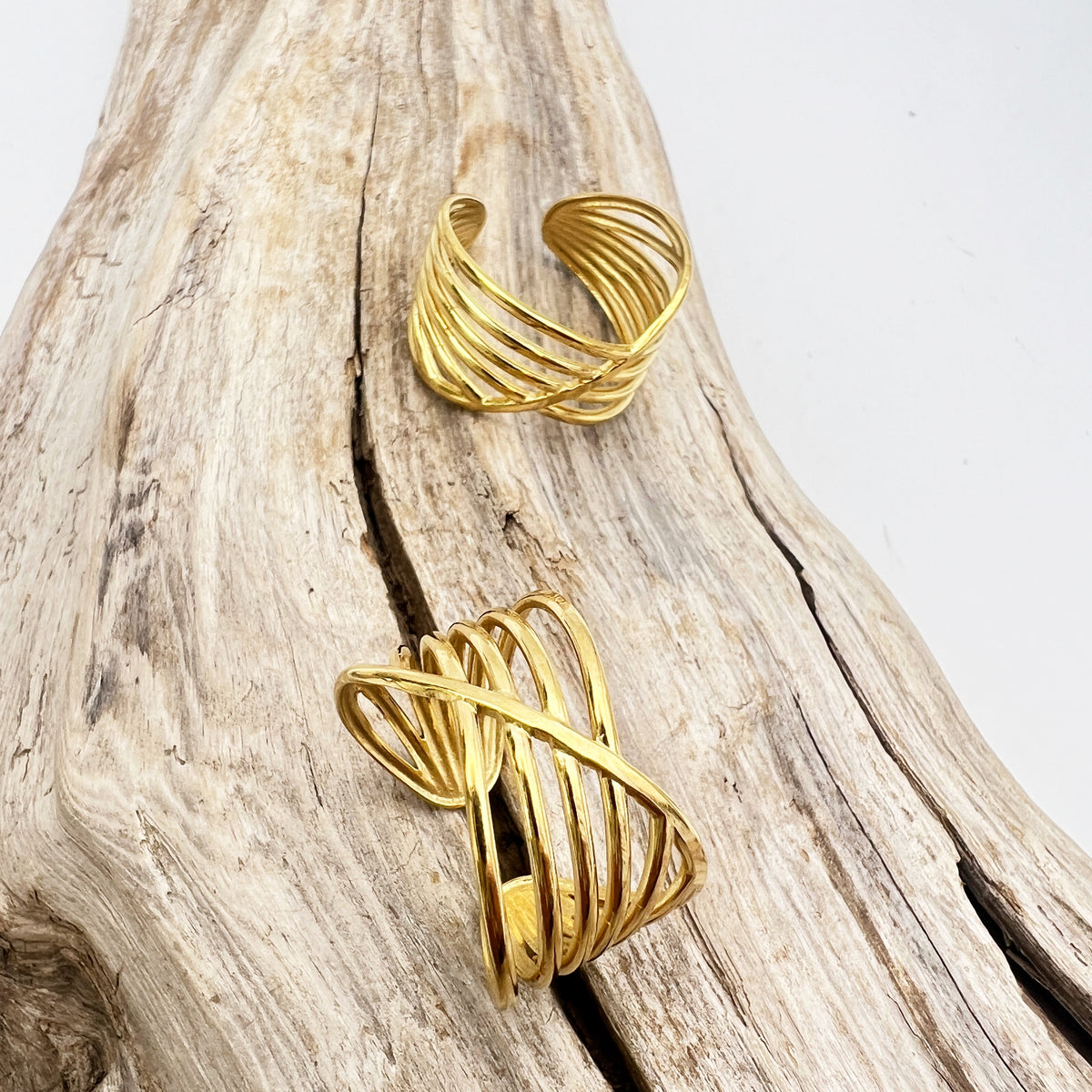 Adjustable stainless steel rings with gold and white design, displayed on a wooden branch.