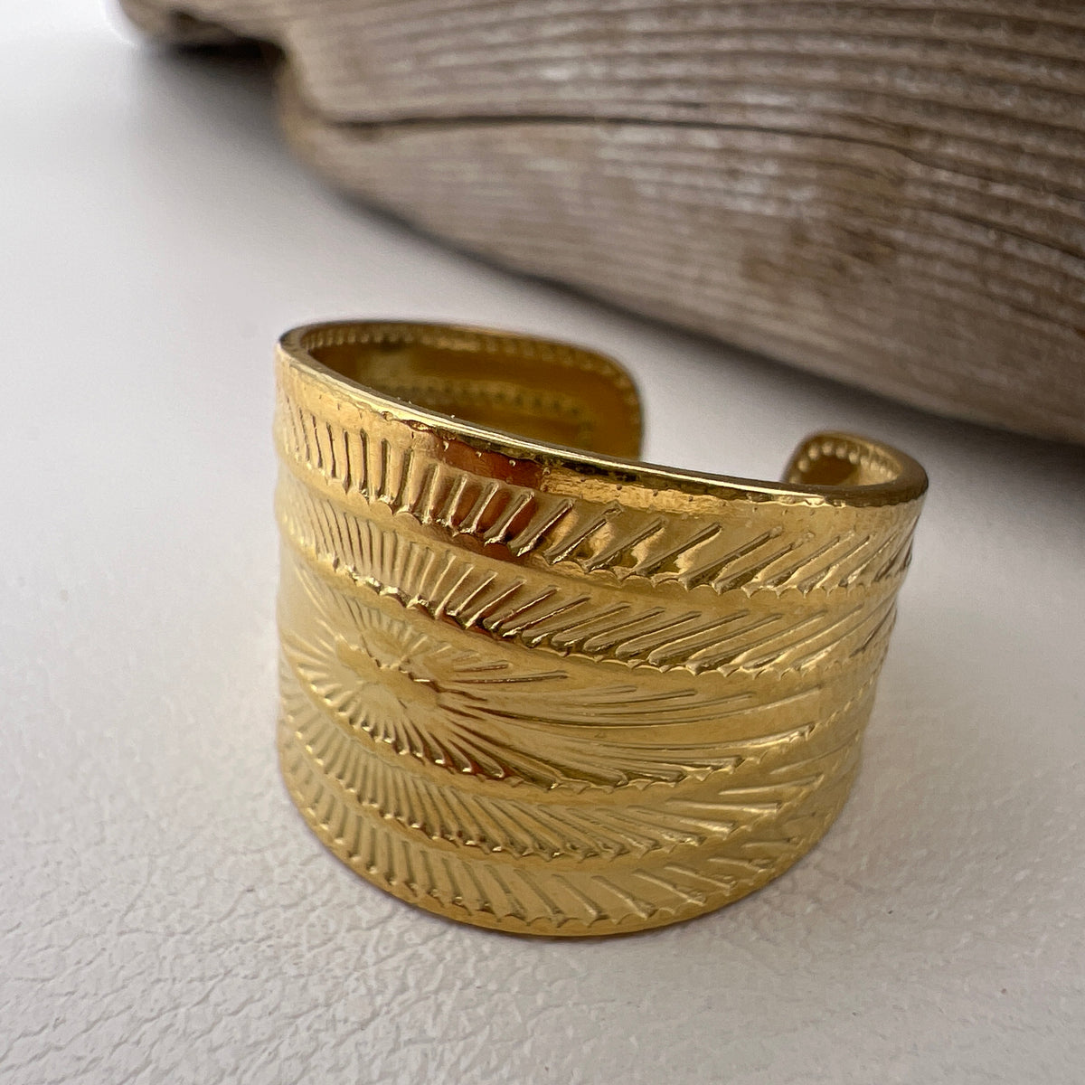 Gold cuff ring with sun design on a textured surface