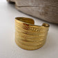 Gold cuff ring with sun design on a textured surface