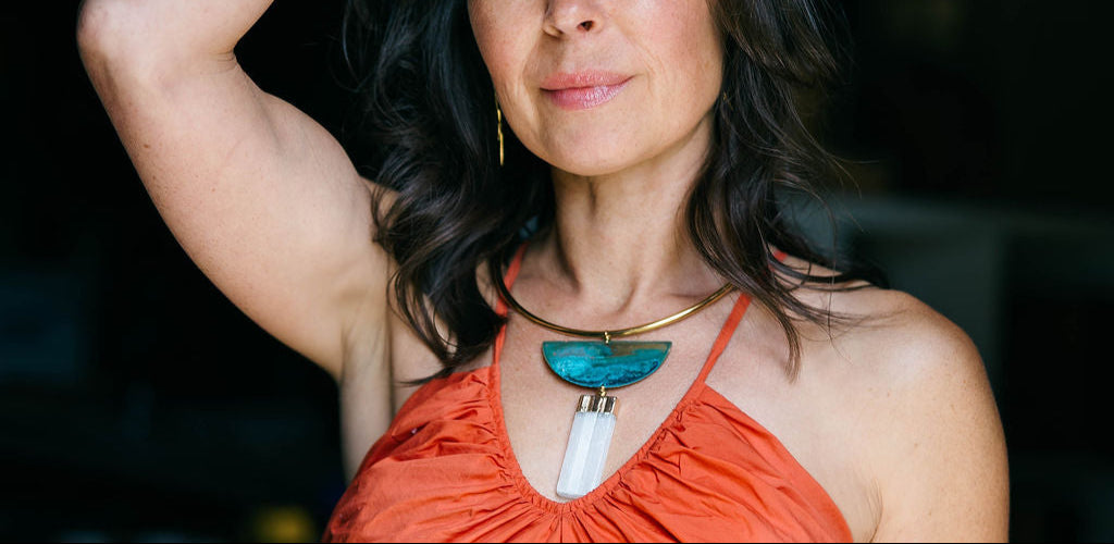 woman wearing an orange top with a golden collar necklace adorned with a turquoise patina moon and a selenite