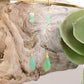 Green teardrop earrings with gold hooks on a wooden surface with a succulent plant.