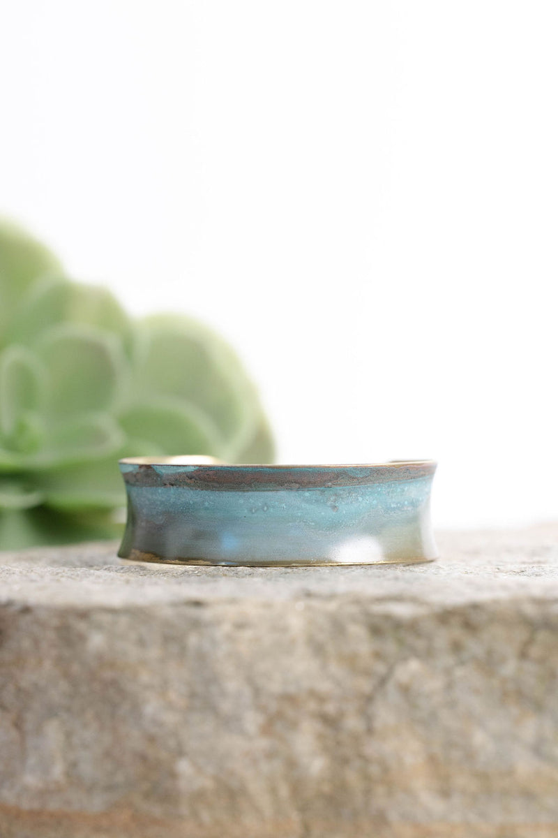 patina coated concave bracelet with turquoise hues on a rock
