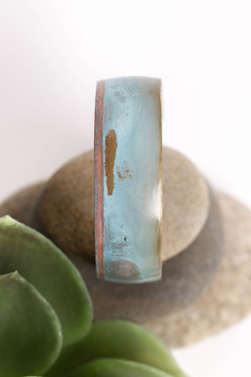 patina coated concave bracelet with turquoise hues on a rock
