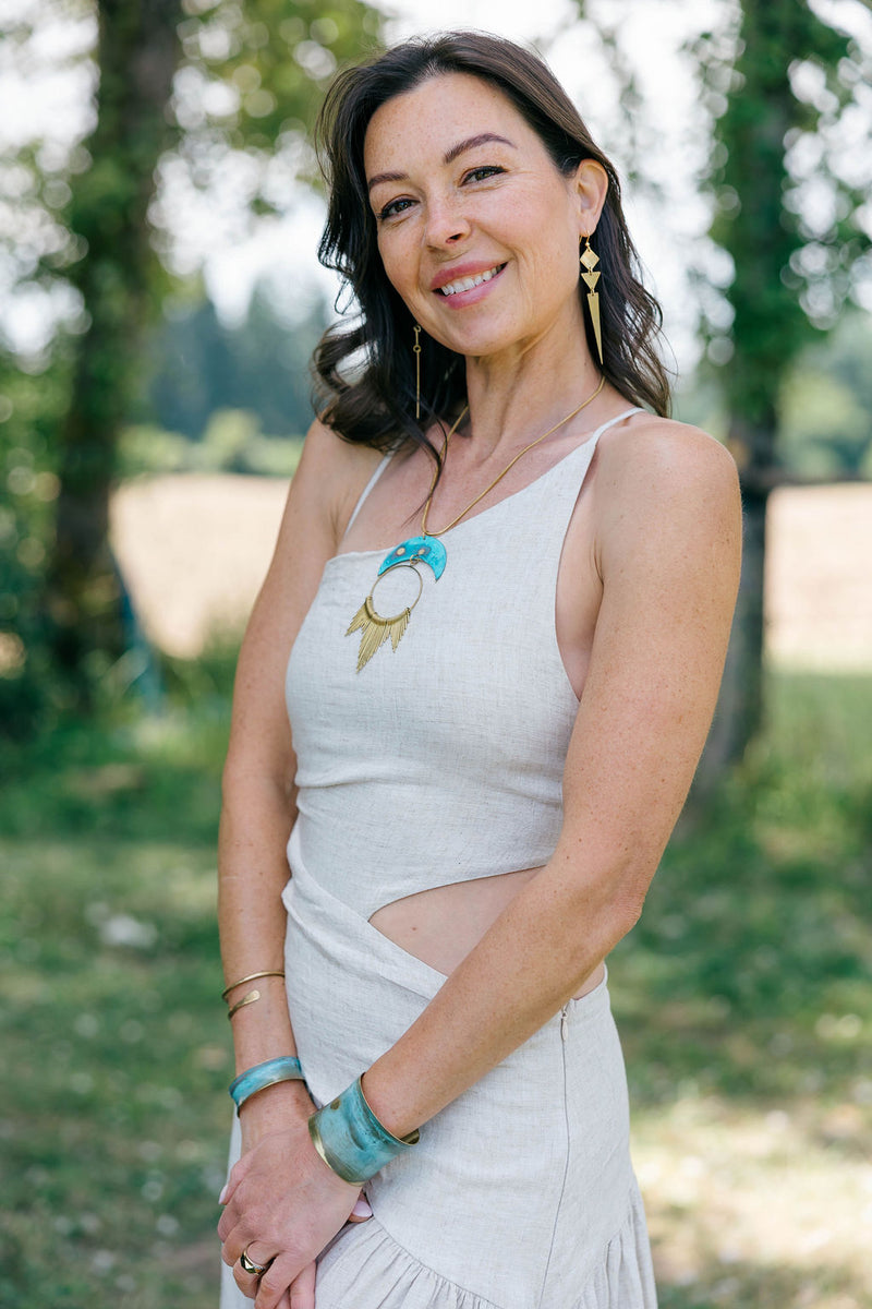 Woman smiling wearing a linen dress and golden spike earrings with brass diamond, triangle and long triangle spike in nature
