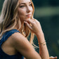 teenager girl in a blue dress sitting outdoors with a blurred green background wearing a hammered twisted golden bracelet