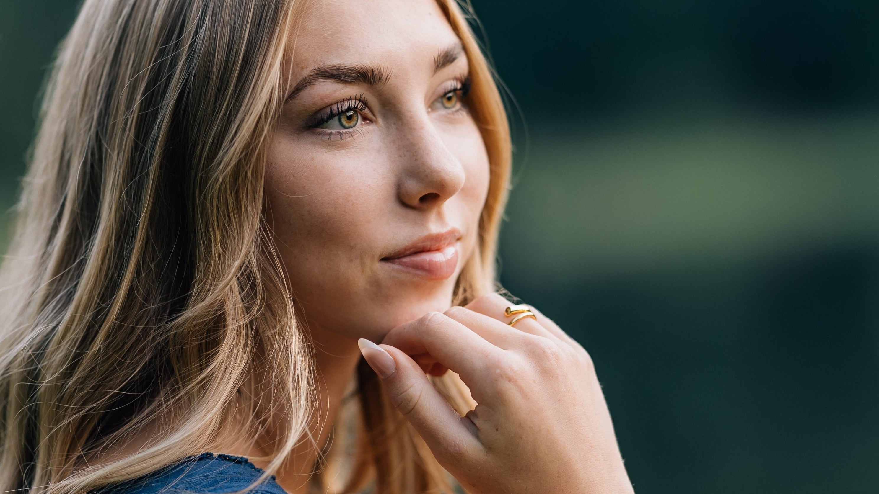 teenager girl in a blue dress sitting outdoors with a blurred green background wearing a hammered twisted golden bracelet
