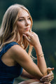 teenager girl in a blue dress sitting outdoors with a blurred green background wearing a hammered twisted golden bracelet
