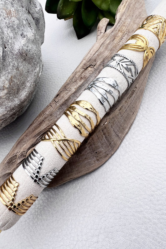 Adjustable stainless steel rings with gold and white design, displayed on a wooden branch.