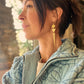 woman wearing golden Geometric dangle earrings and blue quilted jacket