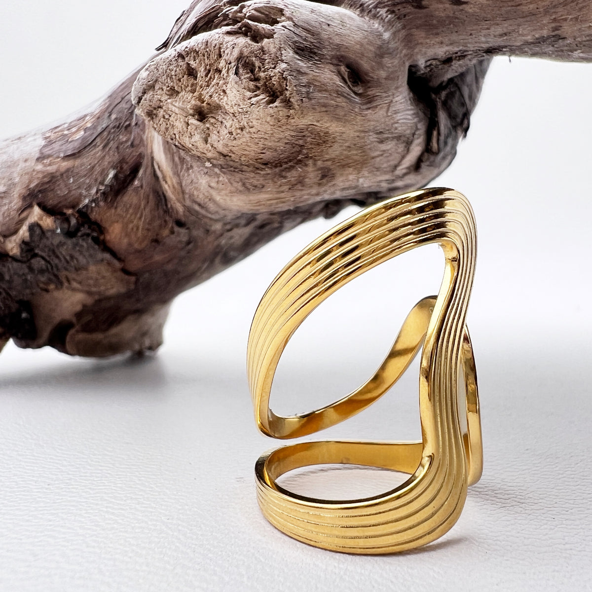Gold wave ring on a white surface with a piece of driftwood.