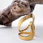 Gold wave ring on a white surface with a piece of driftwood.