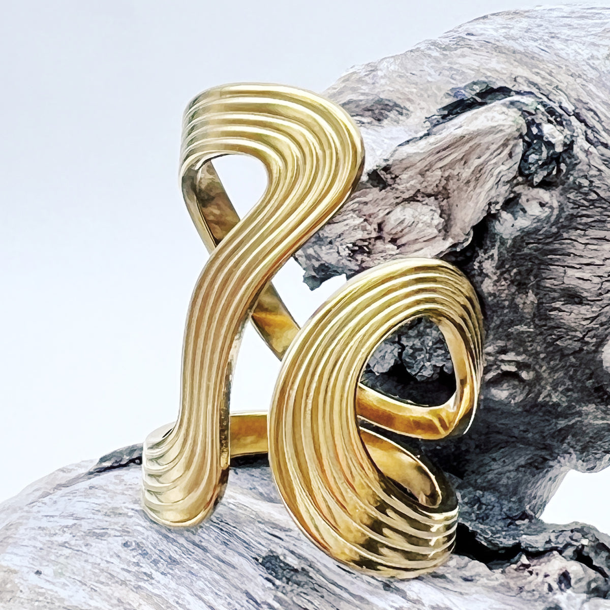 Gold ring with a wavy design on a wooden surface
